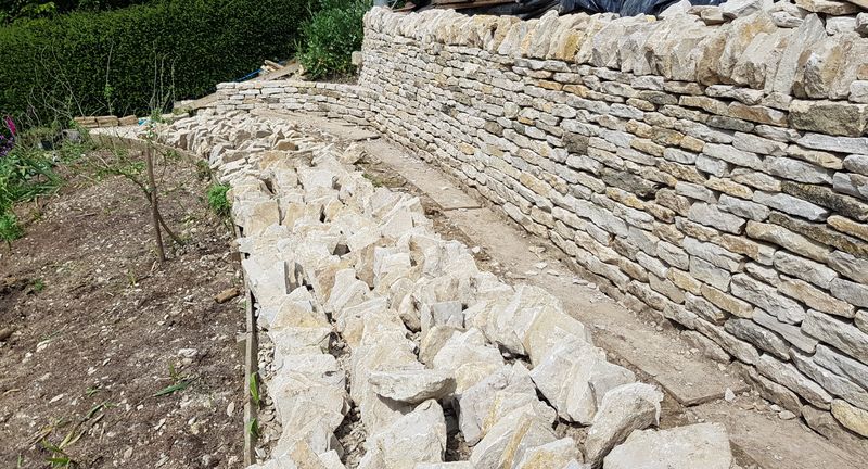 Long curved retaining wall with stone laid out for the next course
